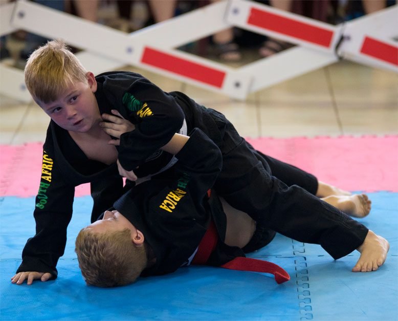 Duas crianças de kimono preto lutando no solo