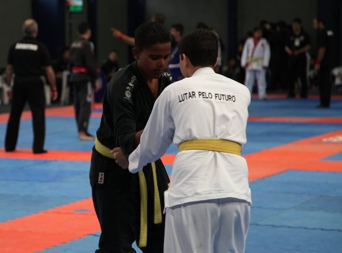Dois jovens de faixa amarela em disputa de pegada; um deles veste kimono com a frase Lutar pelo Futuro
